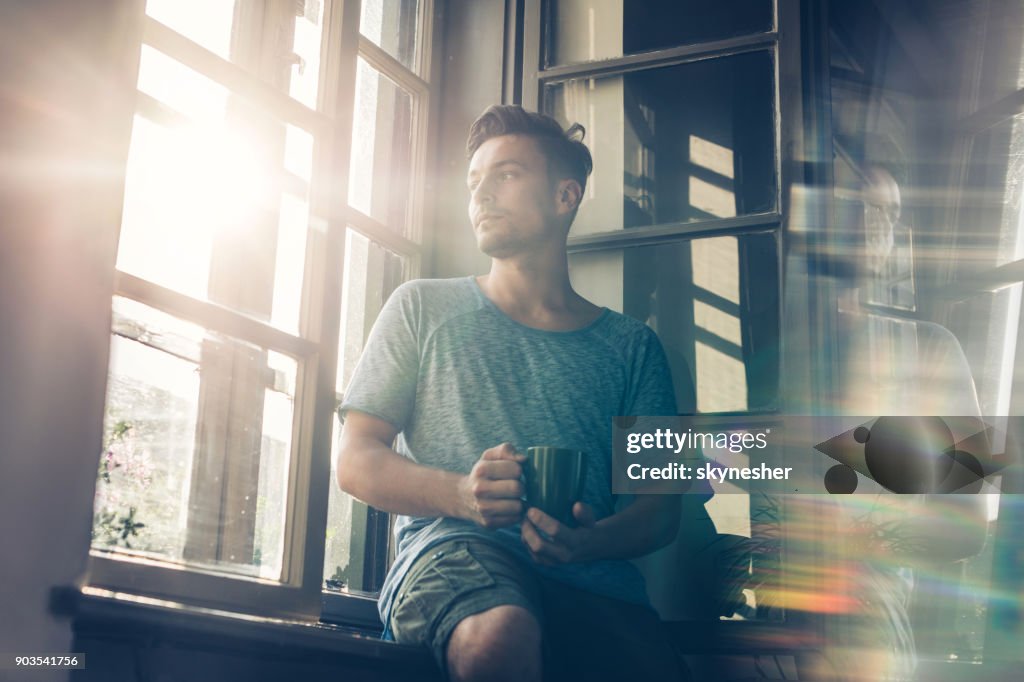 Below view of pensive man with coffee cup by the window.