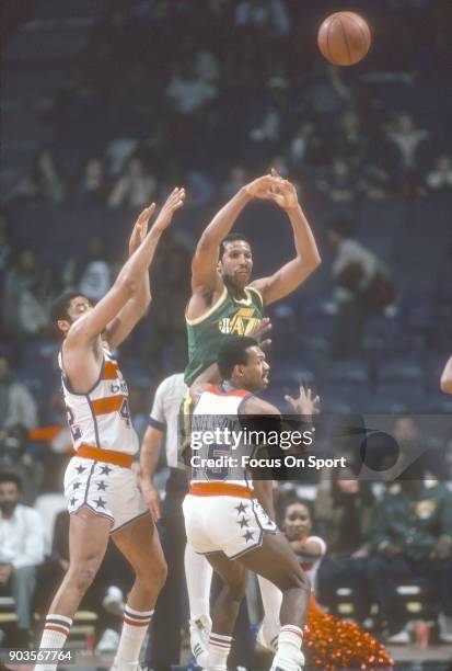 Adrian Dantley of the Utah Jazz passes the ball over the top of Frank Johnson and Greg Ballard of the Washington Bullets during an NBA basketball...