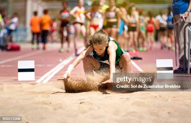 blonde girl with pigtail landing on the sand in long jump - track and field event stock-fotos und bilder