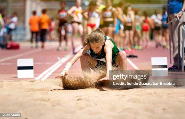 blonde girl with pigtail landing on the sand in long jump - verspringen stockfoto's en -beelden