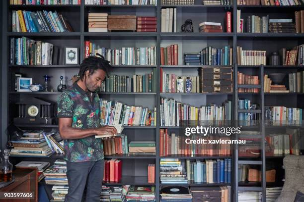 mature man reading book by shelves - black literature stock pictures, royalty-free photos & images