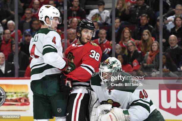 Ryan Hartman of the Chicago Blackhawks and Mike Reilly of the Minnesota Wild watch for the puck next to goalie Devan Dubnyk in the first period at...