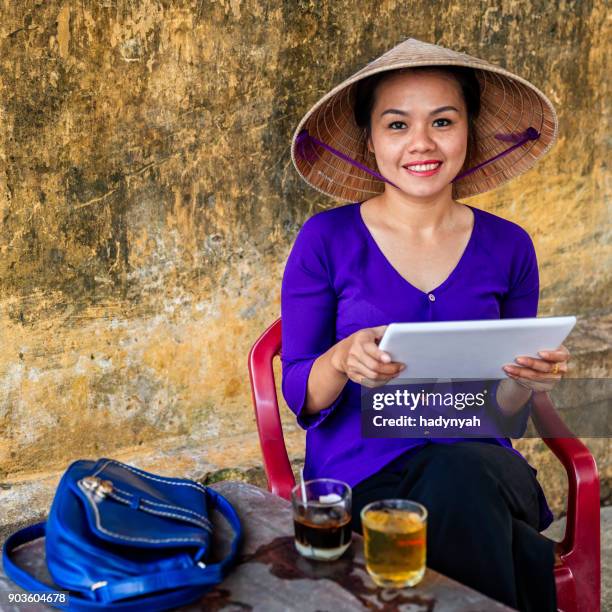 vietnamese woman using digital tablet during coffee break, old town in hoi an city, vietnam - asian style conical hat stock pictures, royalty-free photos & images