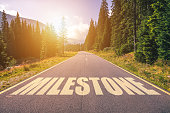 Asphalt road with arrow guideline and Milestone letters painted on the surface. An image of a road milestones are representative of success in the future goal. Road to success with light of the sun