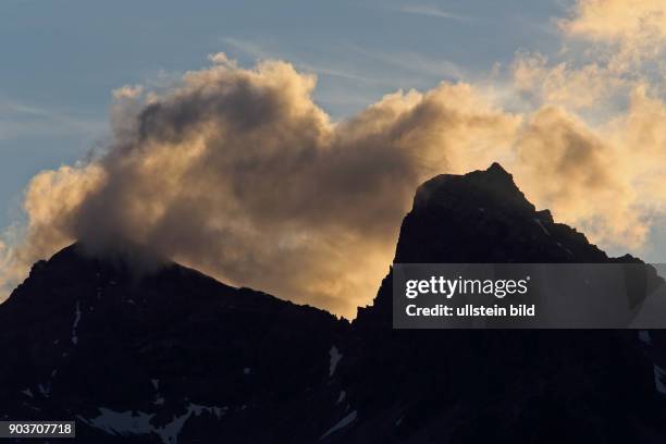 Abendstimmung Berggipfel mit beleuchtetem weissen Wolkenband vor blauem Himmel