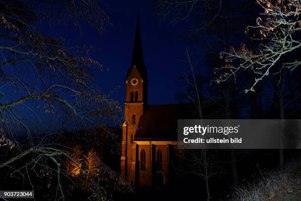 Katholische Kirche Sankt Nikolaus Bad Abbach beleuchtete Kirche vor blauem Abendhimmel zwischen Baumaesten