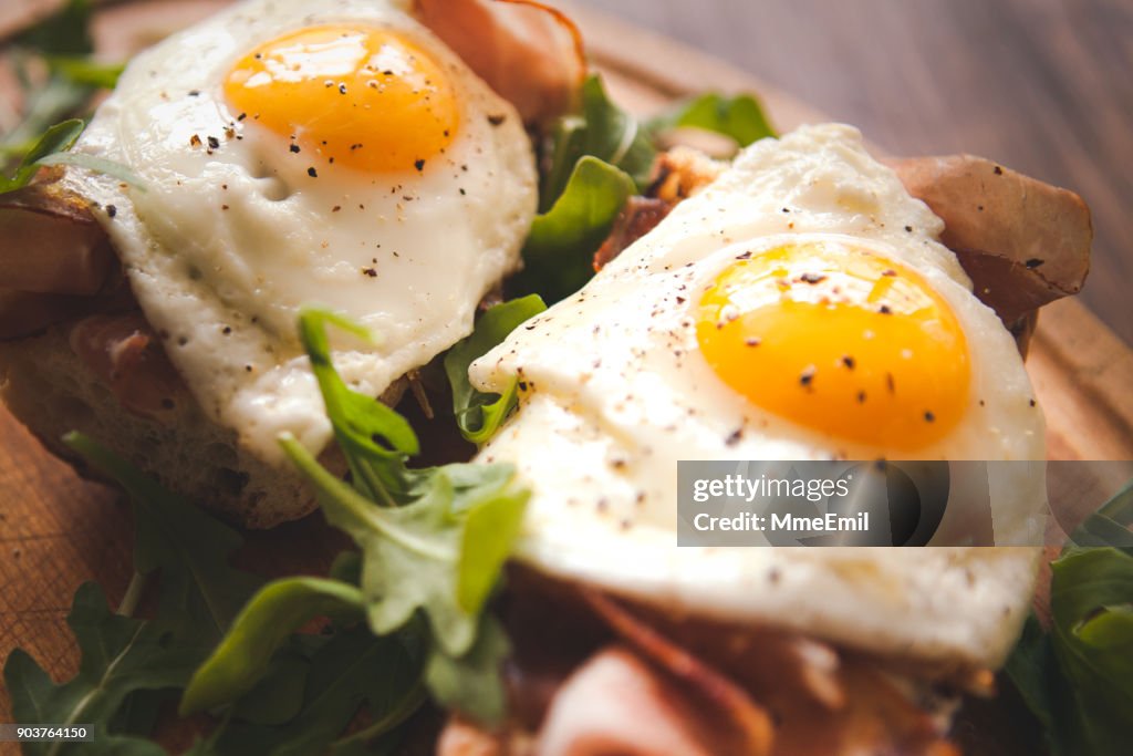 Huevos fritos lado asoleado para arriba en baguette, jamón y rúcula
