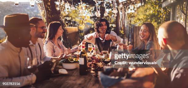 jóvenes amigos multiétnicas, cenar en el restaurante rústico del campo al atardecer - comida del mediodía fotografías e imágenes de stock