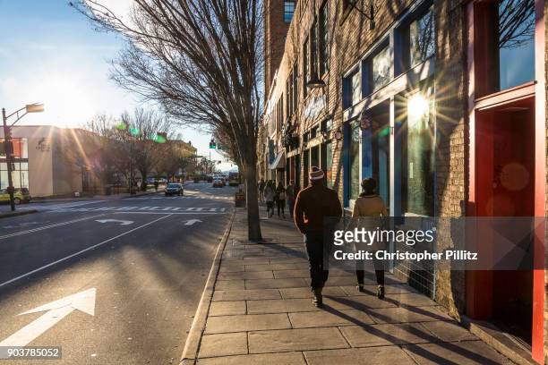 Couple walk along a sun drenched Asheville street, NC.