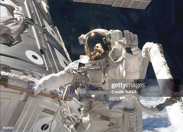 Astronaut James H. Newman, waves at camera as he holds onto one of the hand rails on the Unity connecting module during the early stages of a 7-hour,...