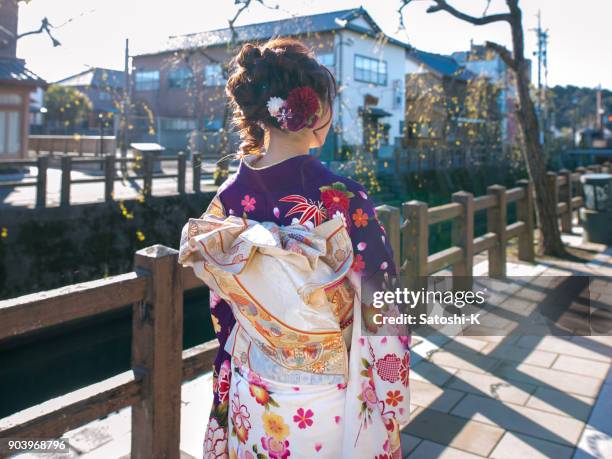 rear view of young woman in furisode kimono walking in traditional japanese town - seijin no hi stock pictures, royalty-free photos & images