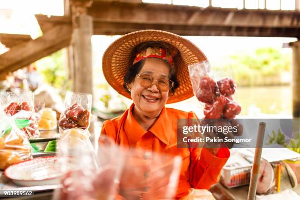 portrait asian senior female smiling and selling many fruit at damnoen saduak floating market - thai ethnicity fotografías e imágenes de stock