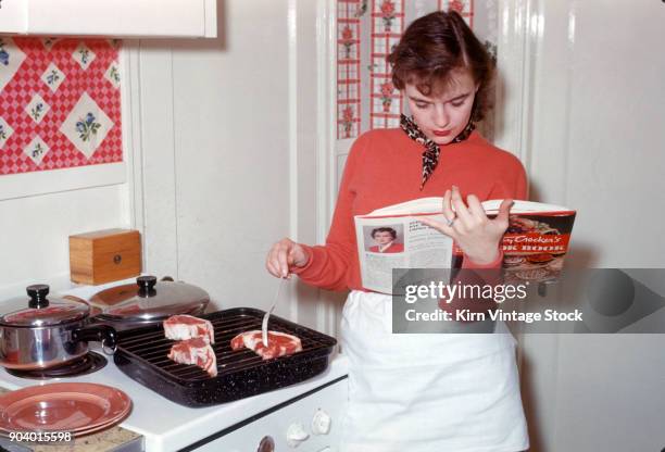 Housewife checks her cookbook while preparing to broil meat.