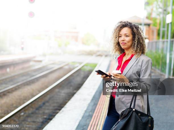 woman with headphones, coffee cup and phone standing on train platform - electronic listening device stock pictures, royalty-free photos & images