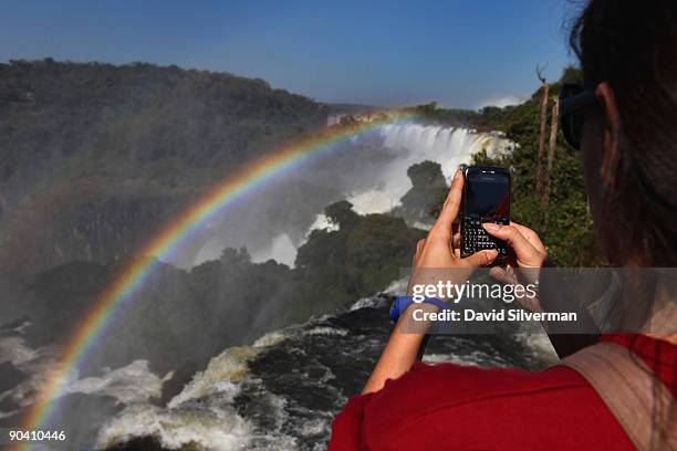 Tourist photographs a pair of rainbows which arch over San Martin Island and which are formed by mist rising from the Iguacu Falls in the Iguazu...