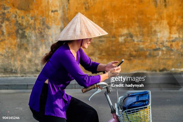 femme vietnamienne à l’aide de téléphone portable sur une bicyclette, la vieille ville de hoi an ville, vietnam - vietnam photos et images de collection
