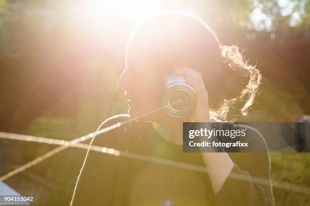 cans communication: young woman listens into tin can phone - tin can phone stock pictures, royalty-free photos & images