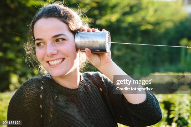 latas de comunicación: mujer joven escucha en teléfono de lata - tin can phone fotografías e imágenes de stock