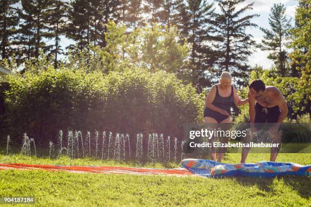 man and his mother playing on a slip and slide in the garden - backyard water slide stock pictures, royalty-free photos & images