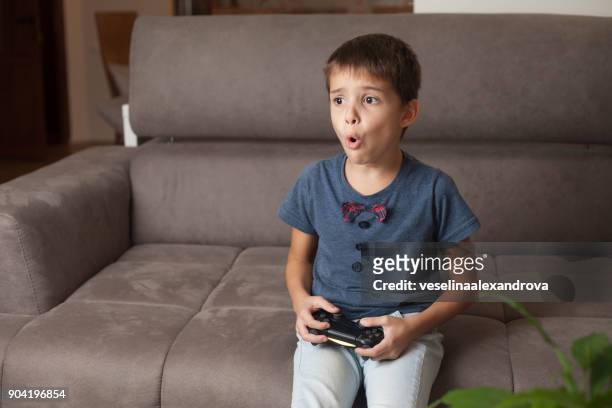 boy sitting on couch playing video games - losing virginity - fotografias e filmes do acervo