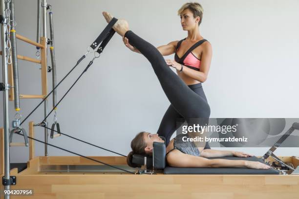 coach assisiting the girl exercising on pilates machine - leg stretch girl stock pictures, royalty-free photos & images
