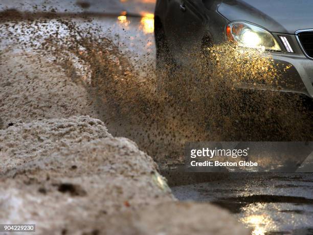 Cars splash through a flooded Cambridge Park Drive adjacent the Alewife MBTA station in Cambridge, MA as warming temperatures melt the previous...