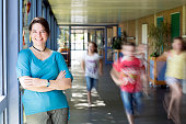 portrait of female teacher, leaning at corridor wall, running children in background