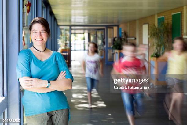porträtt av kvinnliga lärare, lutande på väggen i korridoren, körs barn i bakgrunden - portrait of teacher and student bildbanksfoton och bilder