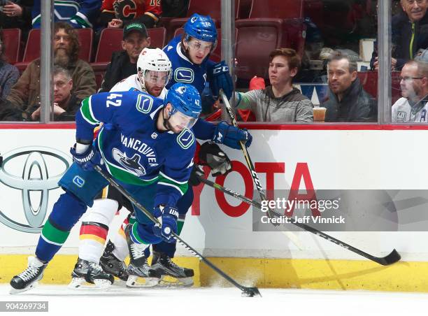 Jake Virtanen of the Vancouver Canucks and TJ Brodie of the Calgary Flames look on as Alexander Burmistrov of the Vancouver Canucks skates up ice...