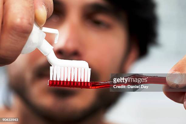 man applying toothpaste to brush - toothpaste stock-fotos und bilder