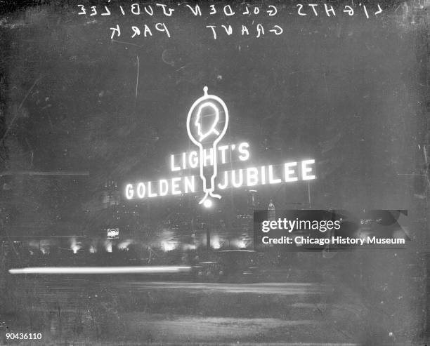 Image of a neon sign for Light's Golden Jubilee sitting in Grant Park, viewed at night, celebrating the 50th anniversary of Thomas Edison's...