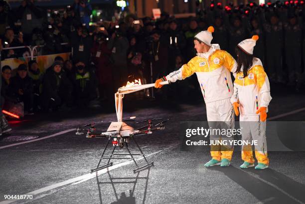Torchbearers pass the Olympic flame to a drone during the PyeongChang 2018 Torch Relay in Seoul on January 13, 2018. Cheering crowds welcomed the...