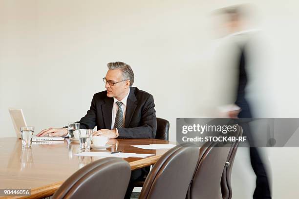 businessman in conference room with person in background passing by, munich, bavaria, germany - rf business stock-fotos und bilder