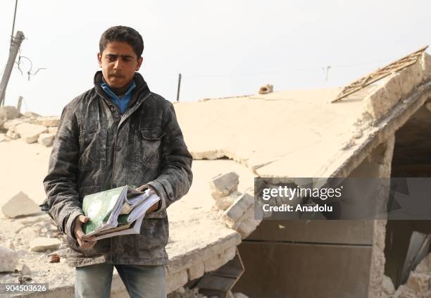 Syrian boy collects his school books from the wreckage of a building after an airstrike at Khan al-Sabil village in Idlib, Syria on January 13, 2018....