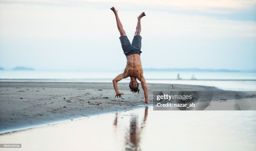 Man standing on one hand at beach.