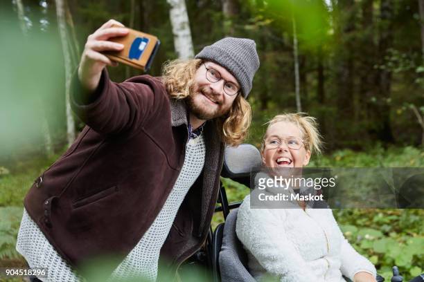 young male caretaker taking selfie with disabled woman in forest - persons with disabilities stock-fotos und bilder