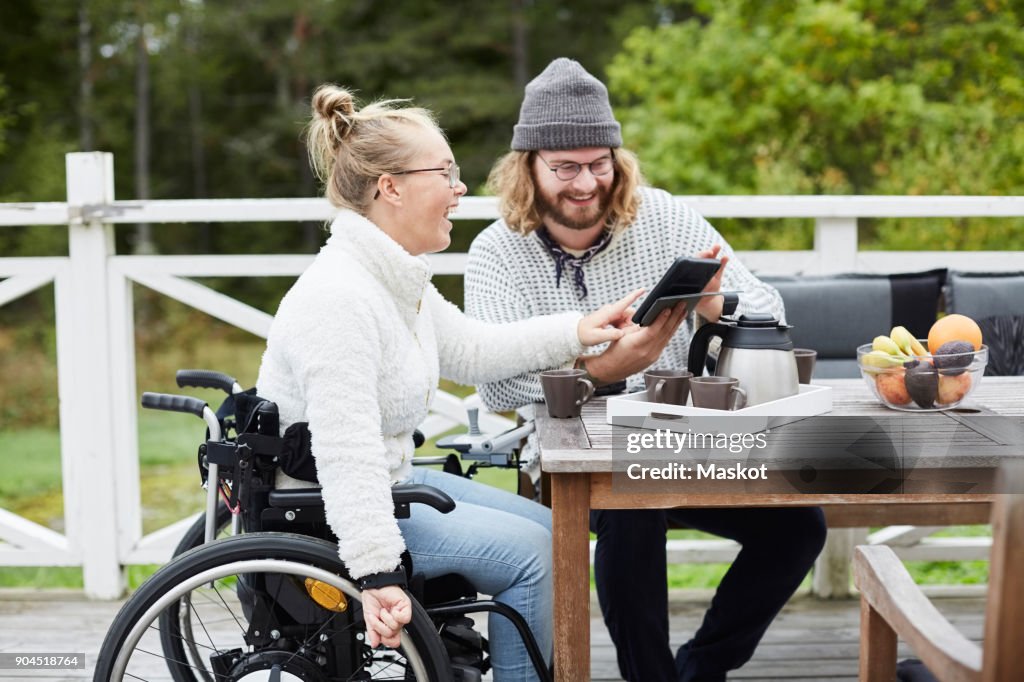 Young male caretaker and disabled woman using digital tablet in yard