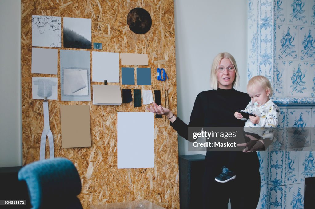 Mid adult businesswoman carrying baby girl while giving presentation in creative office