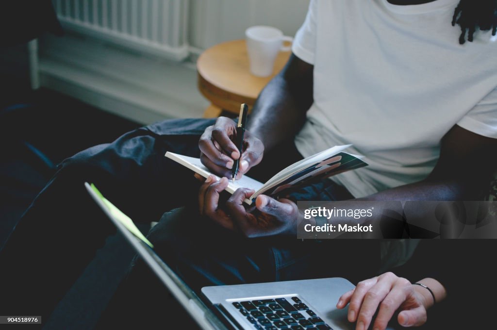 Midsection of businessman writing in diary while colleague using laptop in creative office