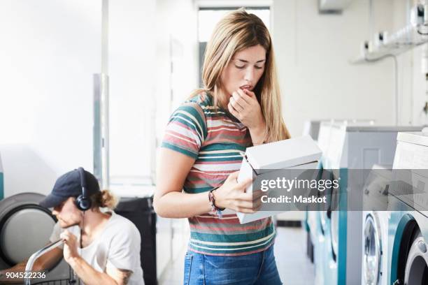 woman reading information on detergent pack while man using washing machine at laundromat - powder laundry detergent stock pictures, royalty-free photos & images