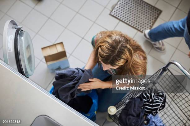 high angle view of woman putting clothes in washing machine at laundromat - waschsalon stock-fotos und bilder