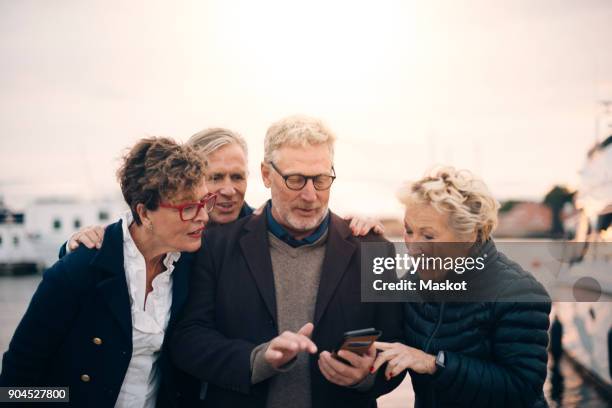 senior male and female friends using smart phone while standing at harbor - senior public transportation stock pictures, royalty-free photos & images