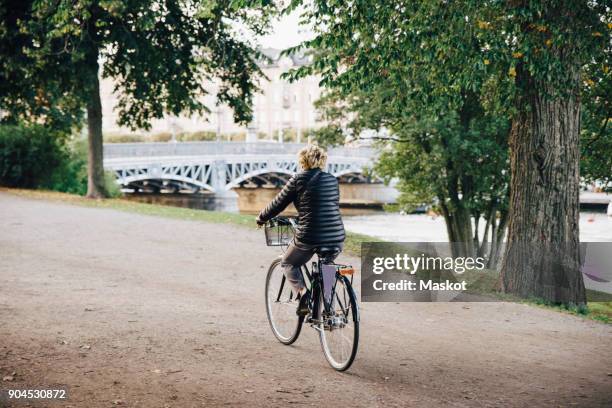 full length rear view of senior woman riding bicycle in park - djurgarden stock pictures, royalty-free photos & images