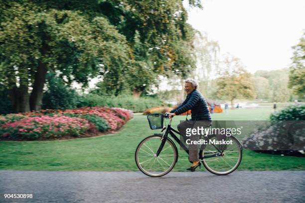 full length side view of smiling senior woman riding bicycle in park - djurgarden stock pictures, royalty-free photos & images