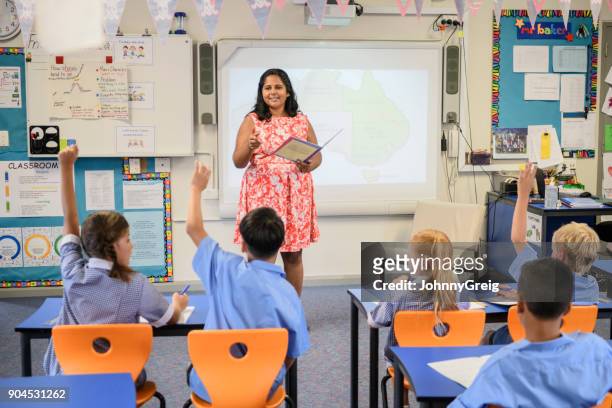 aboriginal school teacher speaking to class with children raising their hands - sydney school stock pictures, royalty-free photos & images
