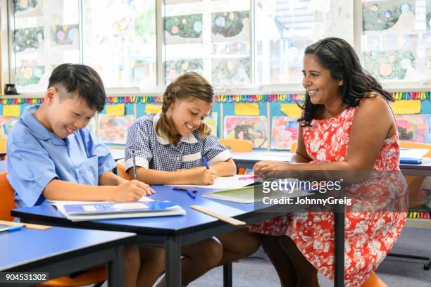 aboriginal teacher smiling at boy and girl working in classroom - native korean stock pictures, royalty-free photos & images