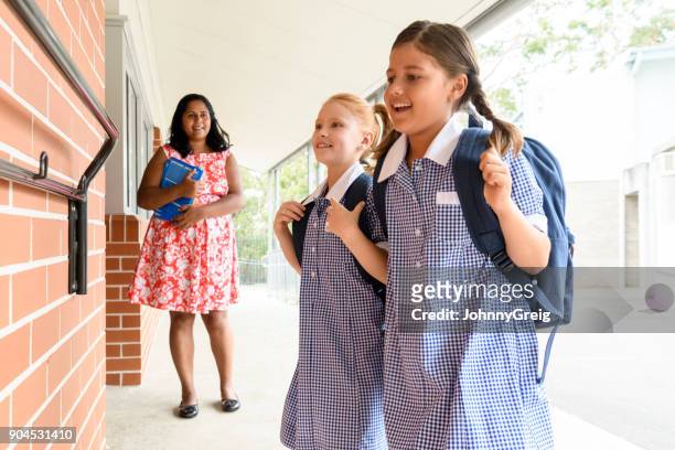 zwei weibliche schulfreunde mit rucksäcken und lehrer im hintergrund - school teacher blue stock-fotos und bilder