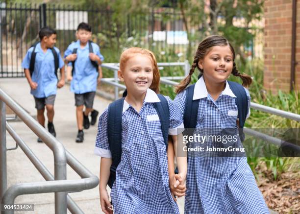 two school girls holding hands on way to school - school uniform stock pictures, royalty-free photos & images