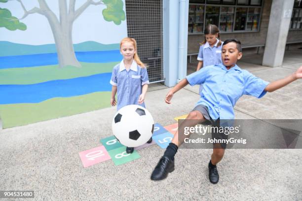 drei kinder spielen im hof junge treten fußball in richtung kamera - children playing in yard stock-fotos und bilder