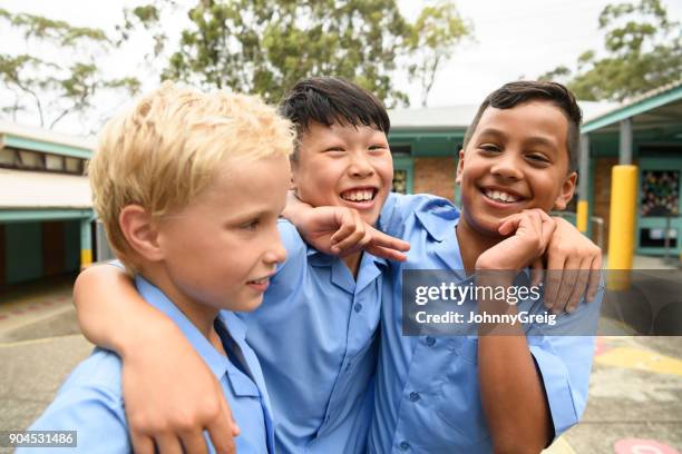 candid portrait of three boys in school playground with arms around each other - australian school stock pictures, royalty-free photos & images